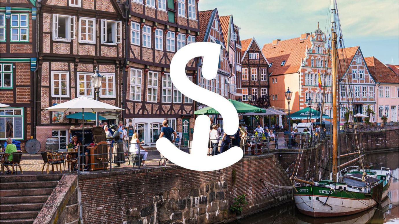 The logo of the city of Stade, a combination of the letter 'S' and an anchor, is displayed in white against a background photo of the city's picturesque historic harbor. The harbor is bustling with lively cafes that surround the water.