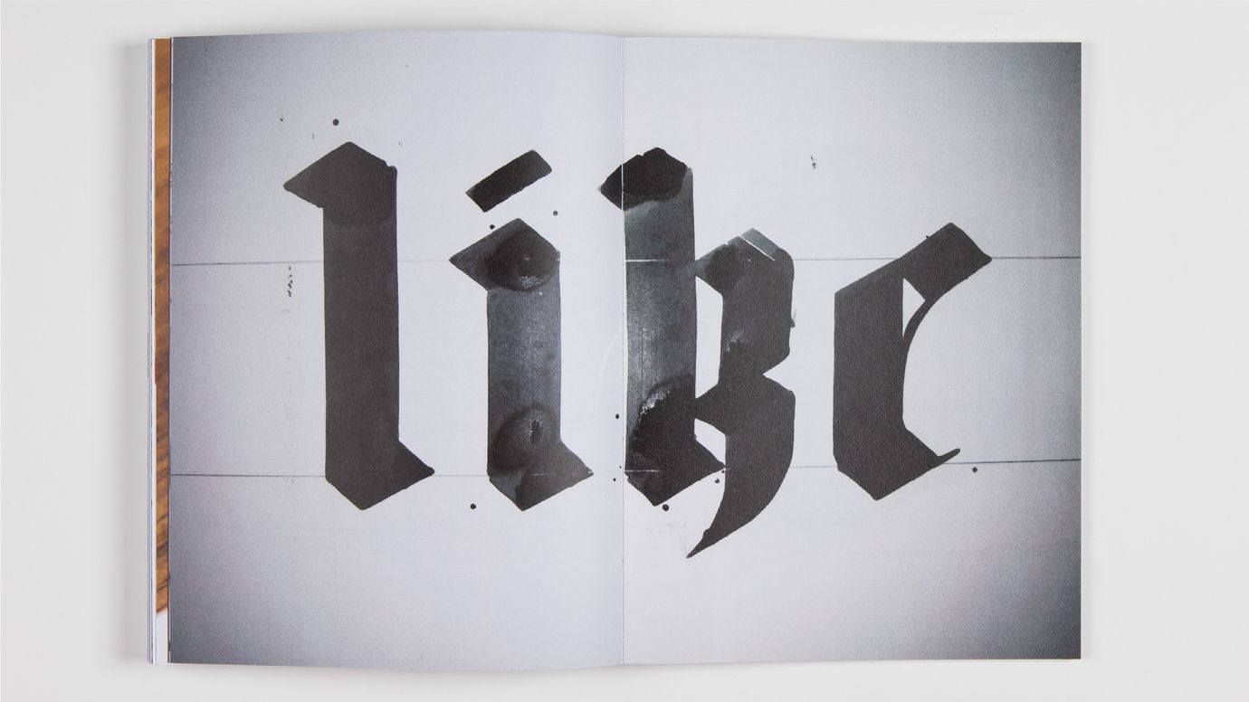 The word ‘like’ is written in huge, brutalist blackletter script across a white double page, with fine guide lines still visible. The ink looks still wet.
